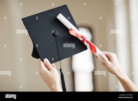 Close Up Of Hands Holding Graduation Cap And Diploma With Red Ribbon At