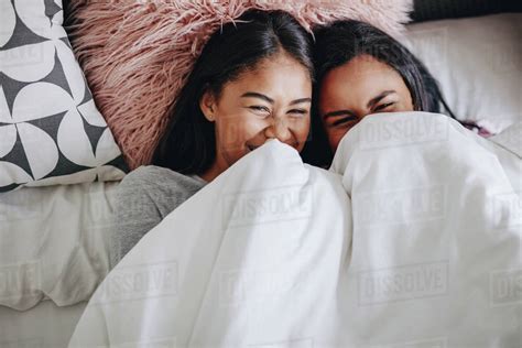 Two Teenage Girls Laughing While Lying On Bed During A Sleepover Top View Of Happy Teenage