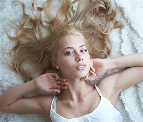 a beautiful blonde woman laying on top of a white blanket