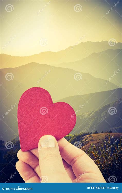 Hand Holding A Heart Shaped Object On Landscape Sunset Stock Image