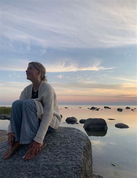 A Woman Sitting On Top Of A Rock Next To The Ocean With Rocks In Front Of Her
