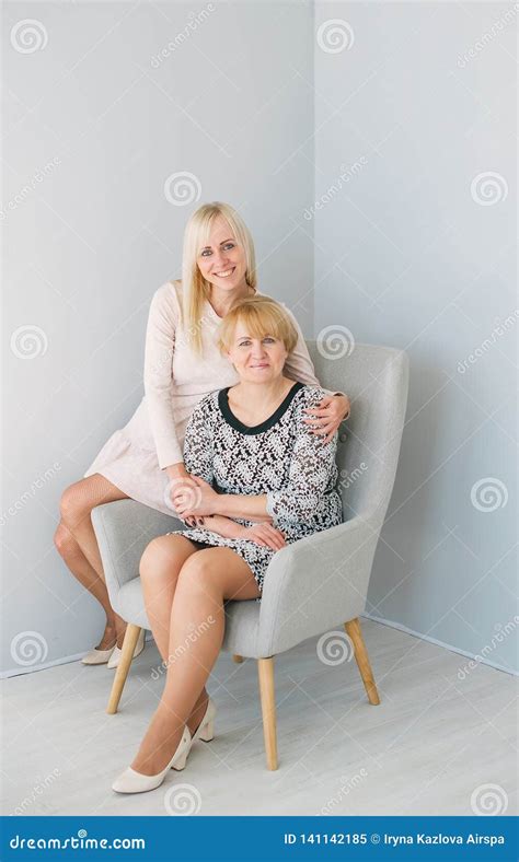 Mature Mother And Blonde Daughter Holding Hands And Siting In Armchair
