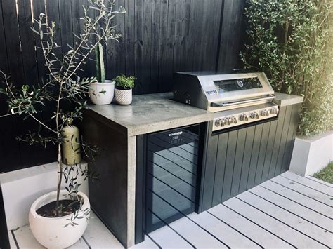 An Outdoor Kitchen With A Grill And Potted Plants On The Counter Top