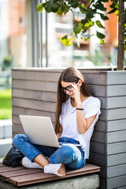 Free Photo Side View Of Young Woman In Eyeglasses Sitting On Bench In Park And Using Laptop
