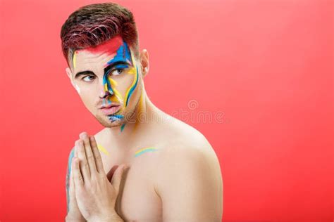 Portrait Of Young Man With Colored Face Paint On Red Background