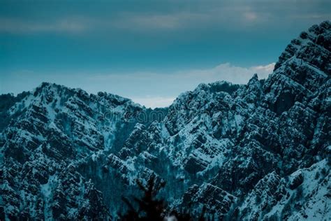 Panoramic Shot Of Snow Covered Jagged Mountain Peaks Under Cloudy Blue