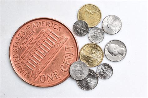 An American One Cent Coin And Some Other Coins On A White Surface With