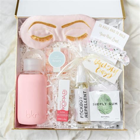 An Open Box With Some Items In It On A White Sheeted Surface Including A Pink Bottle And Gold