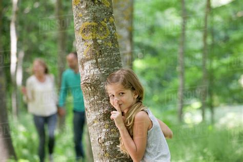 Girl Hiding Behind Tree With Finger On Lips Stock Photo Dissolve