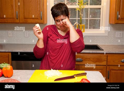Woman Holds Onion And Rubs Tears From Her Eyes In The Kitchen Stock