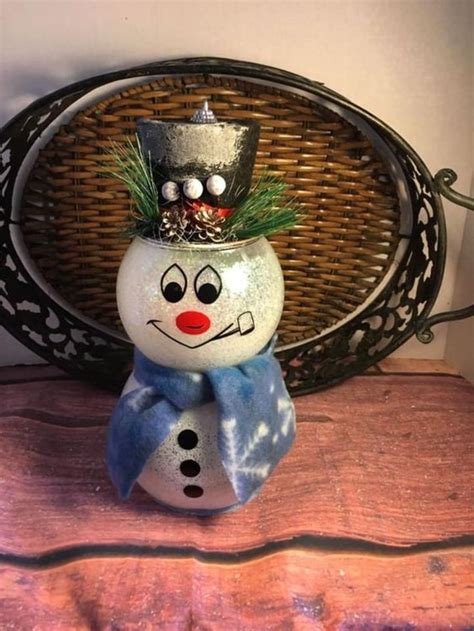 A Snowman With A Hat And Scarf Sitting On Top Of A Wooden Table Next To