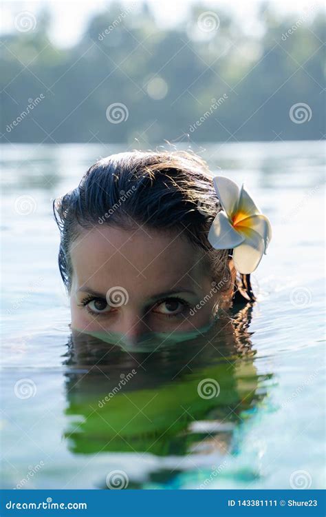 Close Up Of A Female Model Face Half In The Water Of A Pool With A Tropical Flower In A Hear