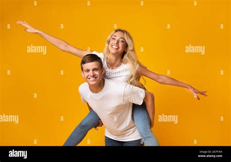 Cheerful Millennial Couple Having Fun Together Over Yellow Background