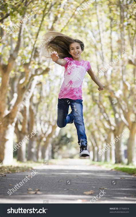 Portrait Of Smiling Tween Girl Jumping On Pathway Between Trees Stock