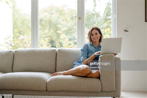 Smiling Mature Woman Sitting On Couch At Home With Laptop Photo Getty