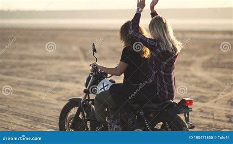 Beautiful Young Woman Motorcyclist With His Girlfriend Riding A Motorcycle In A Desert On Sunset