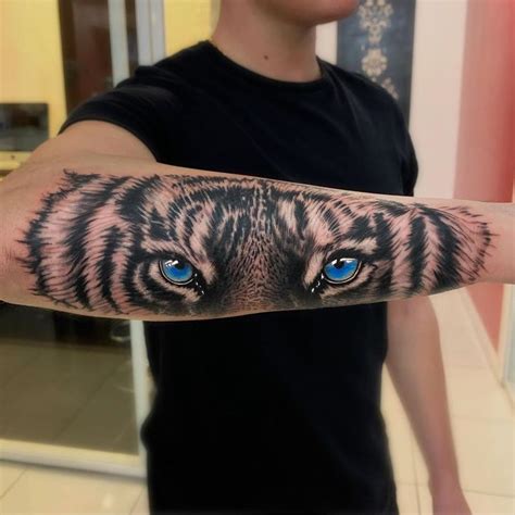 A Man With A Tiger Tattoo On His Arm Holding Up A Blue Eyeball In Front