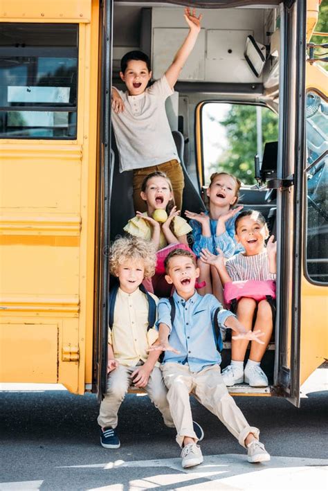 Group Of Adorable Schoolchildren Sitting On Stairs Of School Bus Stock