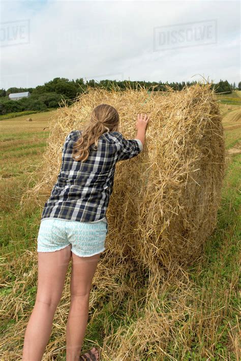 A Teenage Girl Pushes A Large Hay Bale In A Farm Field Kensington