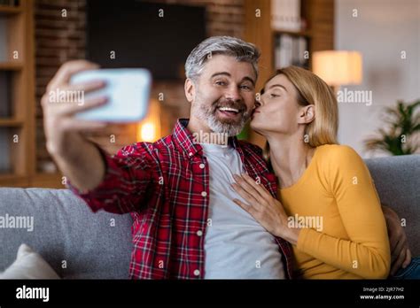 Smiling Middle Aged Caucasian Wife Kisses Husband On Cheek Man With Beard Make Selfie On
