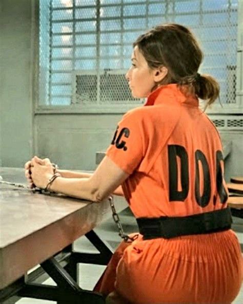A Woman In An Orange Prison Uniform Sitting At A Table With Handcuffs