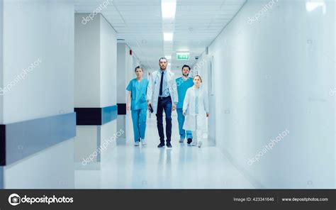 Team Of Doctors Surgeons And Nurses Walk Through Busy Hospital Hallway