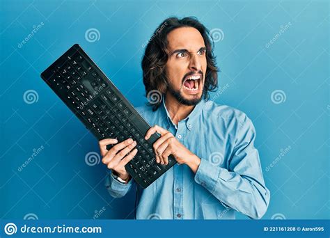 Young Hispanic Man Holding Keyboard Angry And Mad Screaming Frustrated