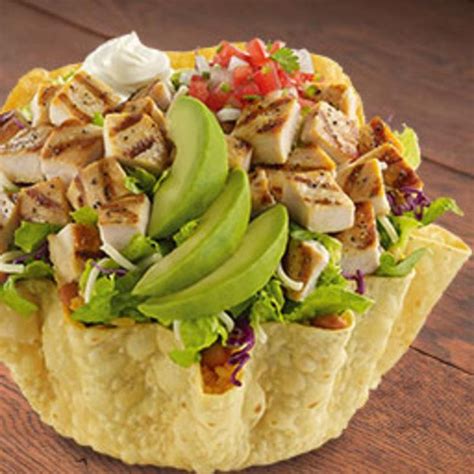A Tortilla Topped With Chicken Lettuce And Avocado On A Wooden Table