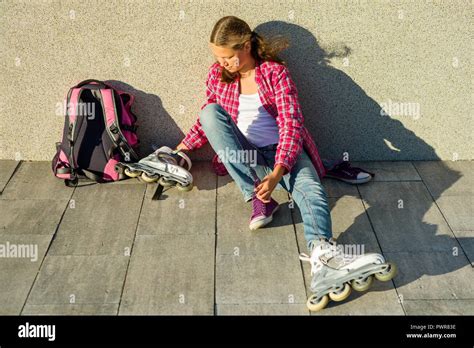 Teen Girl Removes Sneakers And Clothes Roller Skates Outdoor Sits On Wall Background Next To