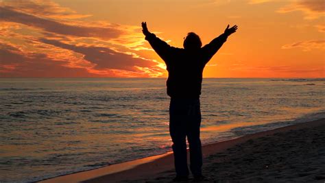 Man With Arms Raised Toward The Heavens Prays At The Beach At Sunset