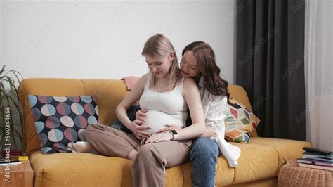 Young Lesbians Relax On The Couch A Young Woman Strokes The Belly Of