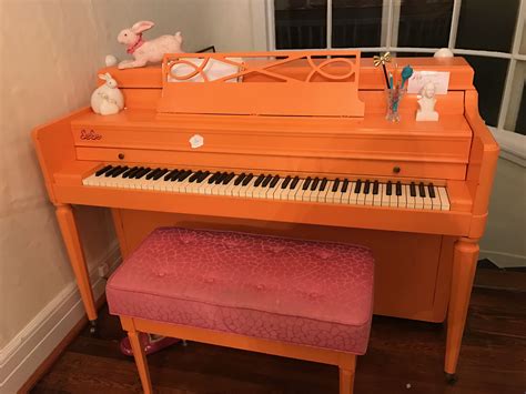 An Orange Piano Sitting In Front Of A Window Next To A Pink Bench With