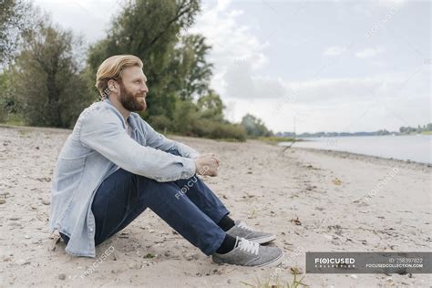 Relaxed man sitting on beach at river — stylish, nature - Stock Photo | #258397822