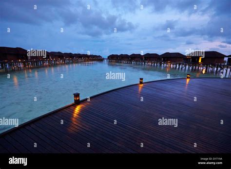 Raised Walkway Leading To Over Water Villas At Night In The Maldives