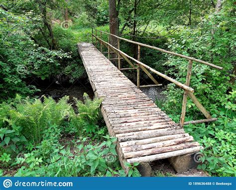 Pedestrian Bridge Over A Stream Built Of Wooden Logs With A One Sided