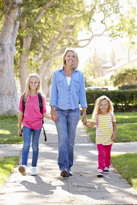 Mother And Daughters Walking To School On Suburban Street Stock Photo
