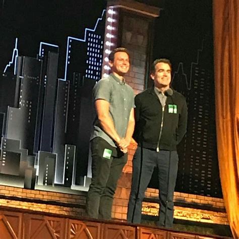 Two Men Standing On Stage In Front Of A Cityscape With Buildings Behind Them