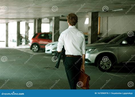 Young Businessman Walking Down The Street Through Parking Stock Photo