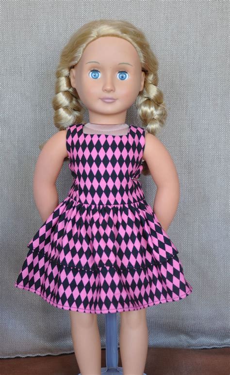 A Doll With Blonde Hair Wearing A Pink And Black Checkered Dress On A Blue Stand
