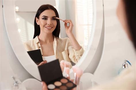 Beautiful Young Woman Applying Makeup Near Mirror Indoors Sponsored