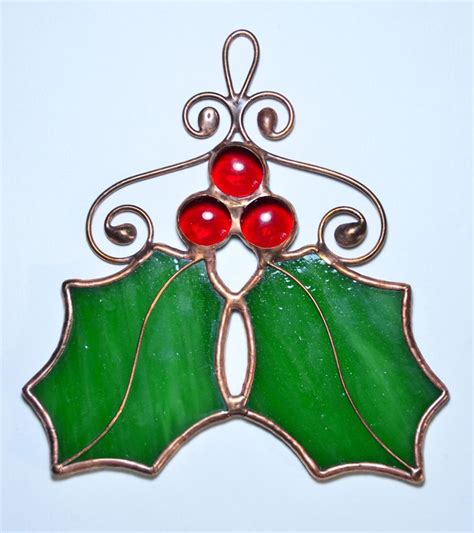 A Stained Glass Christmas Ornament With Holly Leaves And Two Red