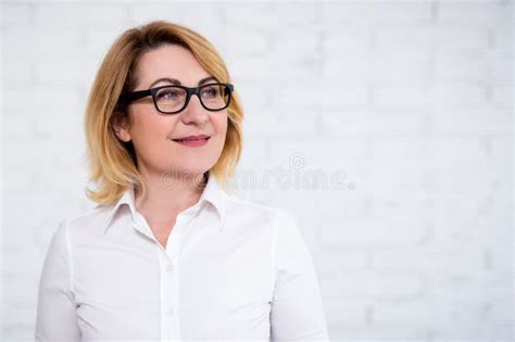 portrait of thoughtful cheerful mature business woman in eyeglasses posing over white wall stock