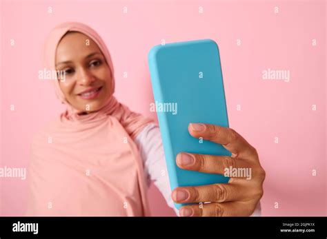 Soft Focus On The Smartphone In Blue Cover In Outstretched Arms Of Arab Muslim Woman Wearing