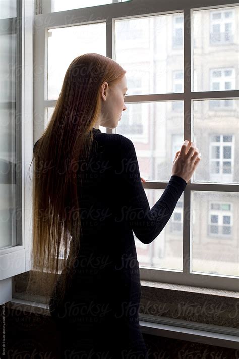 Young Woman Standing At Window Looking Out By Rene De Haan Redhead
