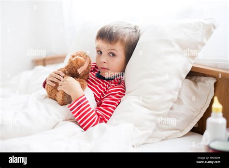 Sick Child Boy Lying In Bed With A Fever Holding Terry Bear With Band