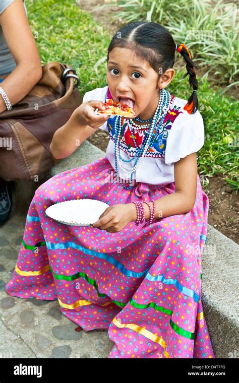 Little Mexican Girl Dressed As Guadalupe In Beautifully Embroidered Skirt Blouse Eating Pizza