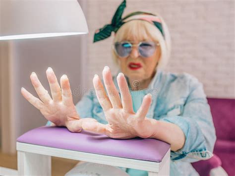 Manicure Master In Blue Gloves Creaming Hands Of Elderly Stylish Woman In Blue Sunglasses And