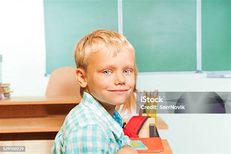 Uśmiech Chłopiec Siedzi Przy Biurku Z Tablica Za Zdjęcia Stockowe I