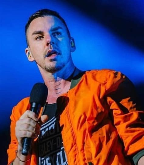 A Man In An Orange Jacket Holding A Microphone