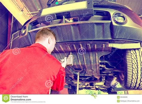 Professional Auto Mechanic In Uniform Working Underneath A Lifted Car